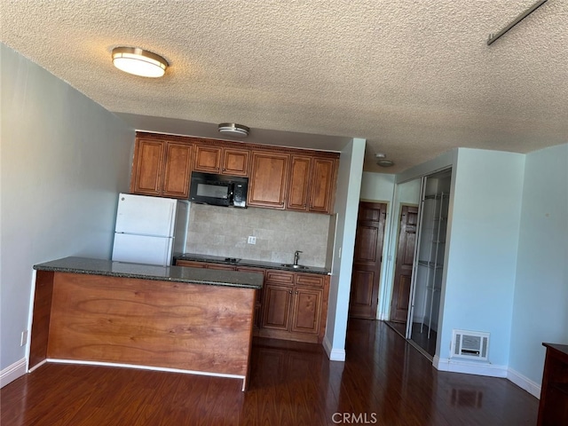 kitchen with black microwave, brown cabinetry, dark wood finished floors, and freestanding refrigerator