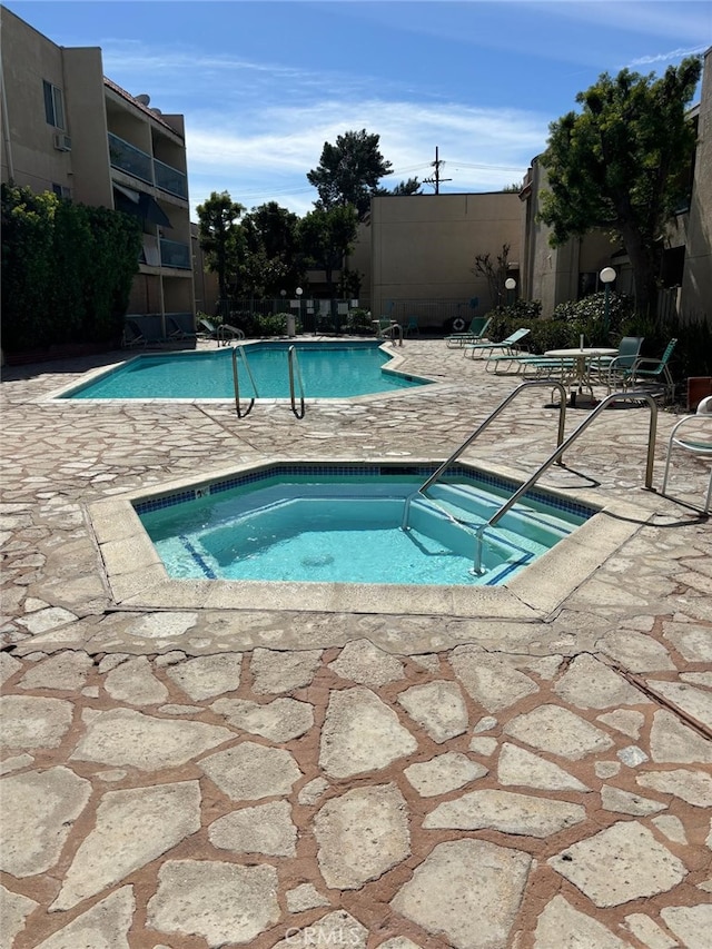 pool with a patio area, fence, and a hot tub