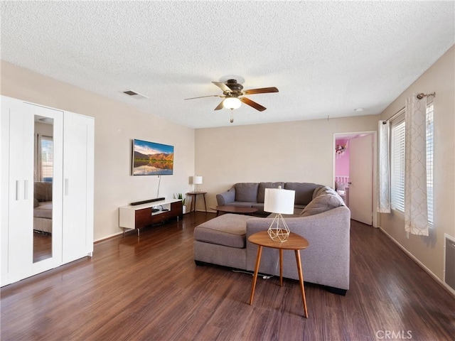 living area featuring dark wood-style floors, visible vents, a textured ceiling, and a ceiling fan