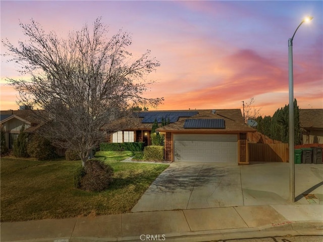 view of front of home featuring an attached garage, solar panels, fence, a yard, and concrete driveway