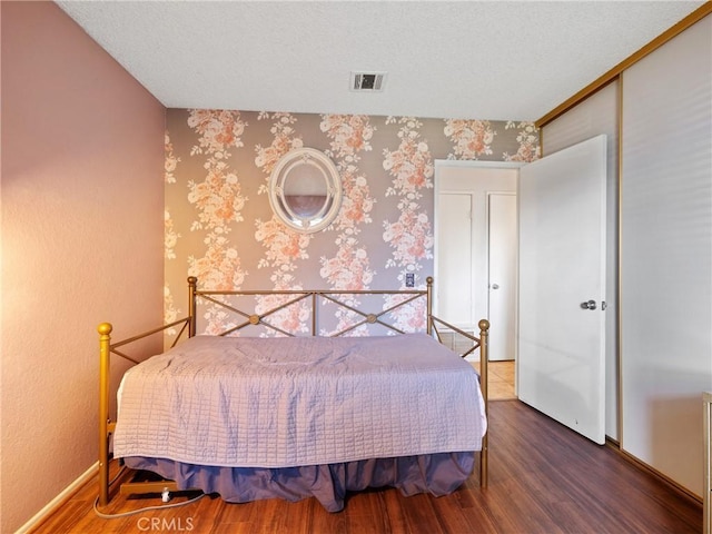 bedroom featuring wood finished floors, visible vents, baseboards, a closet, and wallpapered walls