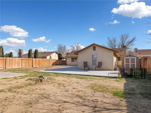 rear view of property featuring a fenced backyard, an outdoor structure, stucco siding, a storage unit, and a patio area