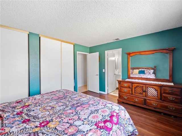 bedroom with a textured ceiling, connected bathroom, wood finished floors, visible vents, and multiple closets