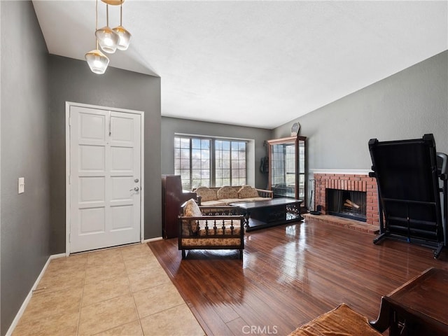 tiled living room featuring a brick fireplace and baseboards