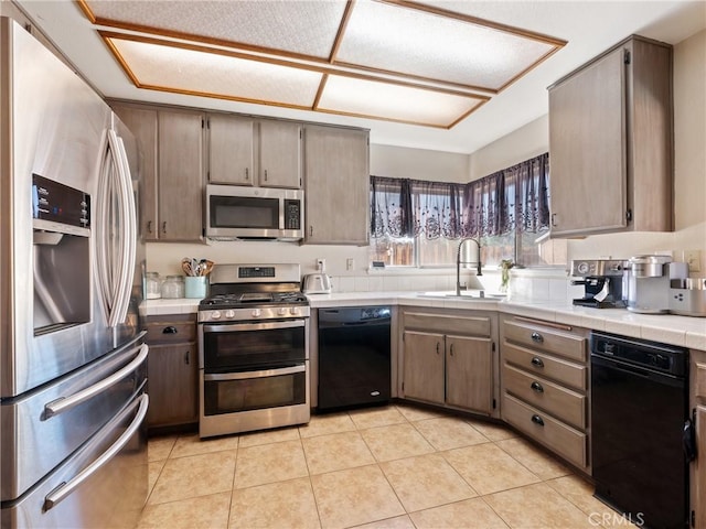 kitchen with appliances with stainless steel finishes, light tile patterned flooring, a sink, and tile countertops