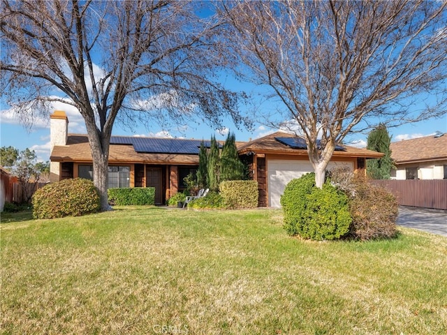 ranch-style home with a garage, fence, a front lawn, and solar panels