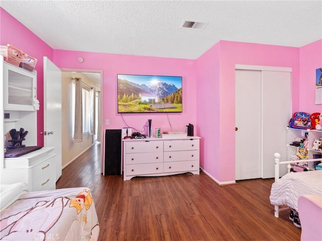 bedroom featuring a closet, visible vents, a textured ceiling, wood finished floors, and baseboards