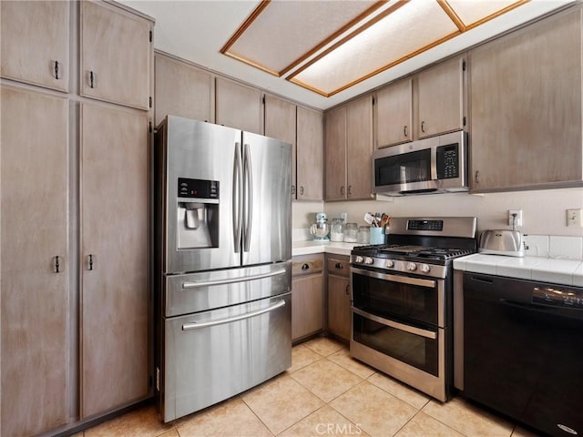 kitchen with appliances with stainless steel finishes, tile counters, and light tile patterned flooring