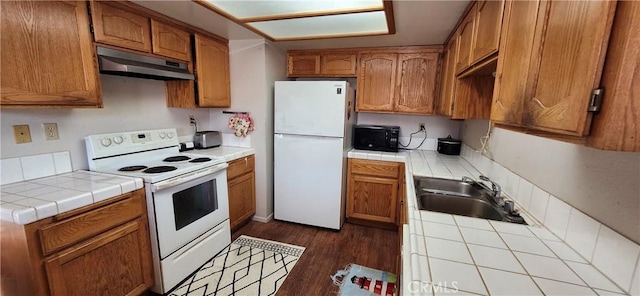 kitchen featuring white appliances, tile counters, brown cabinets, under cabinet range hood, and a sink