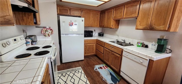 kitchen featuring white appliances, under cabinet range hood, brown cabinetry, and a sink