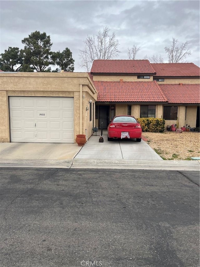 view of front facade featuring a tiled roof, concrete driveway, an attached garage, and stucco siding