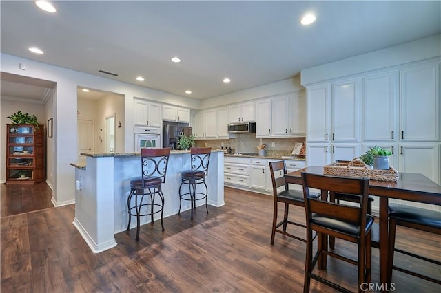 kitchen featuring stainless steel appliances, a kitchen island, visible vents, white cabinets, and dark wood-style floors