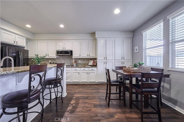 kitchen featuring a breakfast bar area, stainless steel microwave, decorative backsplash, white cabinets, and black refrigerator