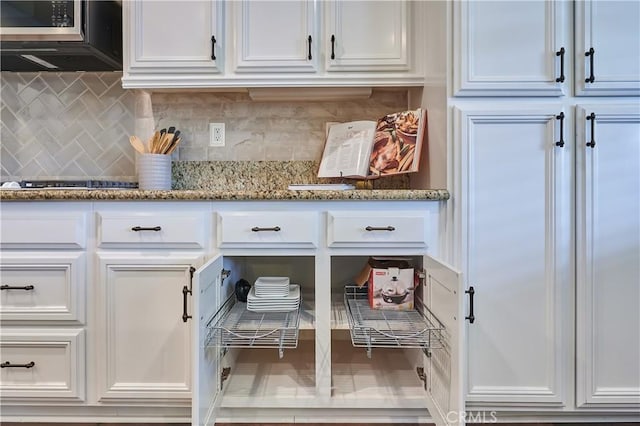 details with tasteful backsplash, stone countertops, white cabinetry, and stainless steel microwave