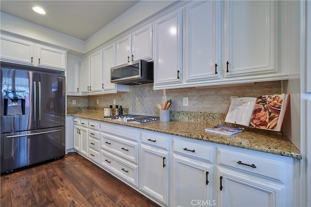 kitchen with stainless steel appliances, white cabinets, light stone counters, and dark wood-style floors