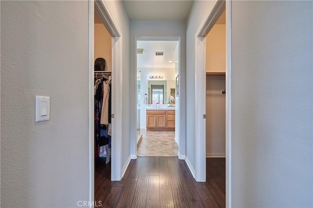 hallway with dark wood-style floors, a textured wall, visible vents, and baseboards