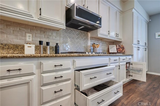 kitchen featuring white cabinets, appliances with stainless steel finishes, dark wood-style flooring, stone counters, and backsplash