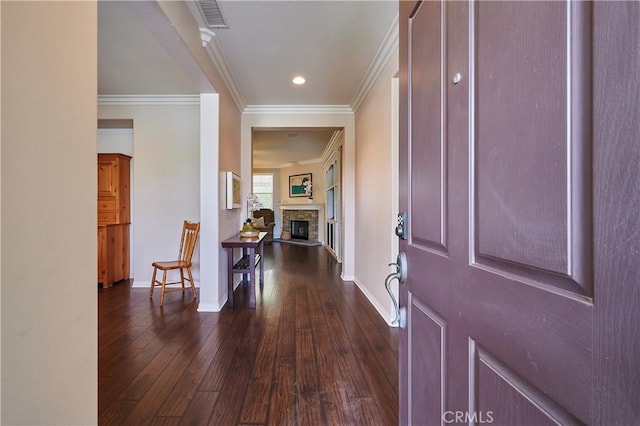 entryway with crown molding, dark wood finished floors, visible vents, a stone fireplace, and baseboards