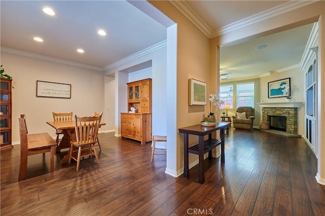 dining area with dark wood-style floors, a stone fireplace, baseboards, and crown molding