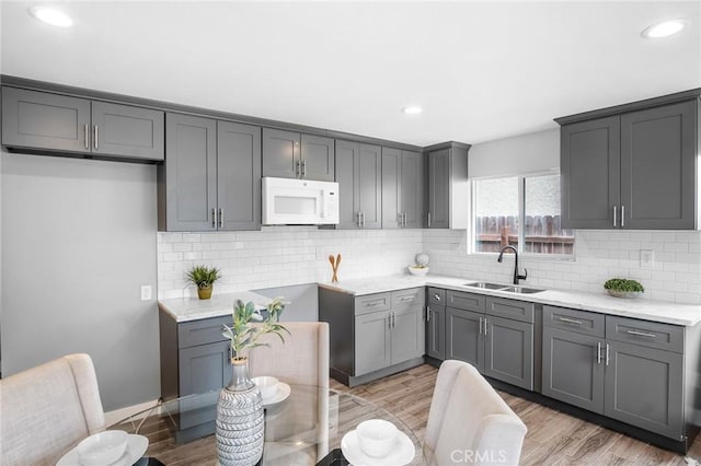 kitchen with light wood finished floors, white microwave, a sink, and gray cabinetry