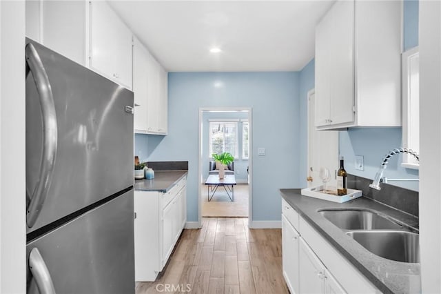 kitchen with light wood-type flooring, dark countertops, a sink, and freestanding refrigerator