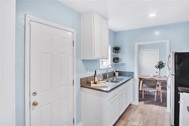 kitchen featuring light wood-style flooring, a sink, freestanding refrigerator, and white cabinets