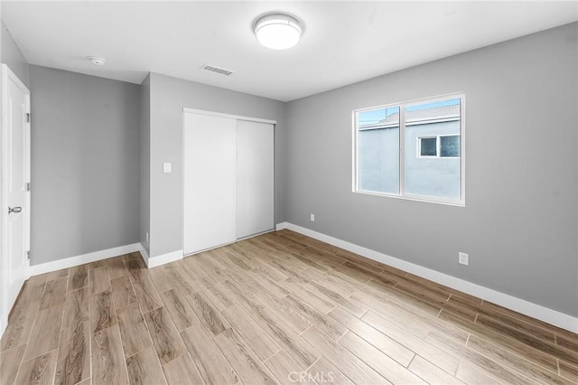 unfurnished bedroom with light wood finished floors, a closet, visible vents, and baseboards