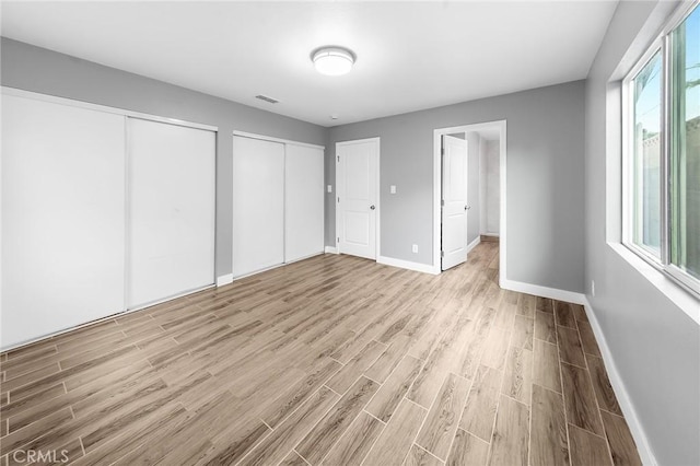 unfurnished bedroom with visible vents, two closets, light wood-style flooring, and baseboards