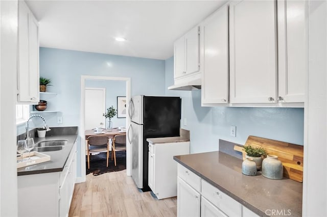 kitchen featuring freestanding refrigerator, dark countertops, a sink, and white cabinetry