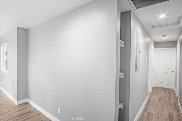 hall with light wood-style floors, attic access, visible vents, and baseboards