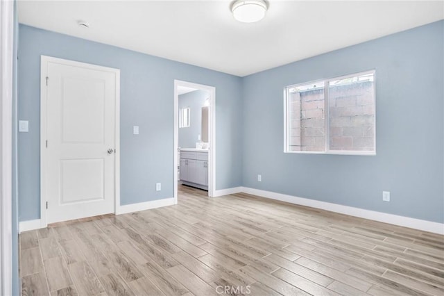 unfurnished bedroom featuring baseboards, connected bathroom, and light wood finished floors