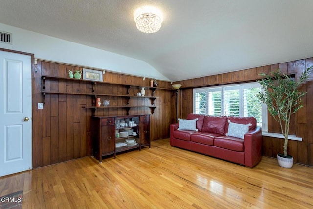 unfurnished living room with lofted ceiling, visible vents, wooden walls, and light wood finished floors