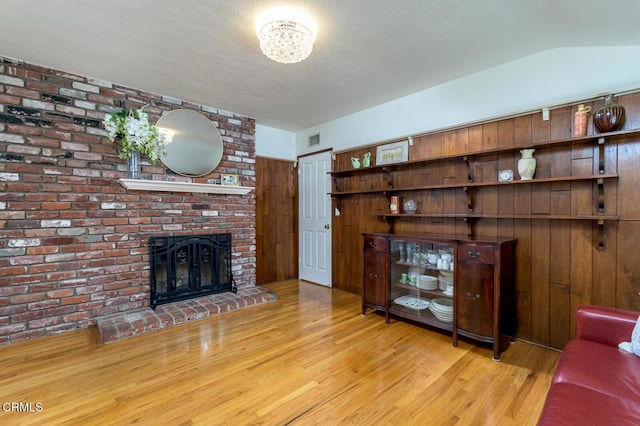 unfurnished living room featuring light wood finished floors, visible vents, lofted ceiling, a textured ceiling, and a brick fireplace