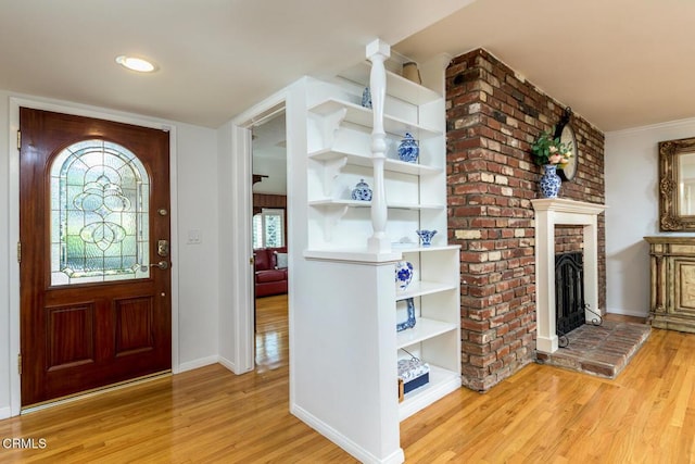 foyer featuring light wood-type flooring, a brick fireplace, and baseboards