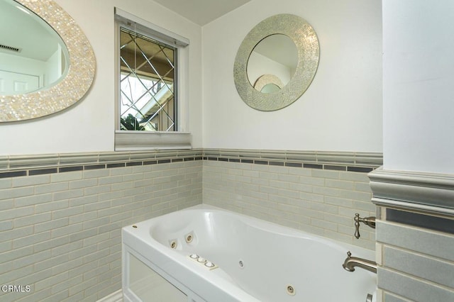 full bathroom with visible vents, a tub with jets, tile walls, and wainscoting