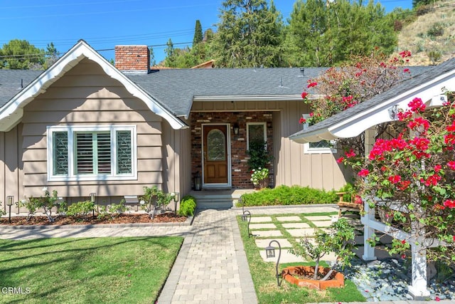 exterior space featuring a lawn, a chimney, roof with shingles, board and batten siding, and brick siding