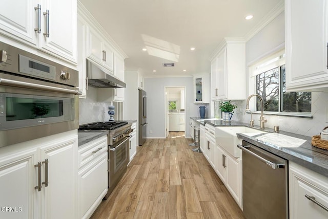 kitchen with under cabinet range hood, appliances with stainless steel finishes, white cabinets, and crown molding