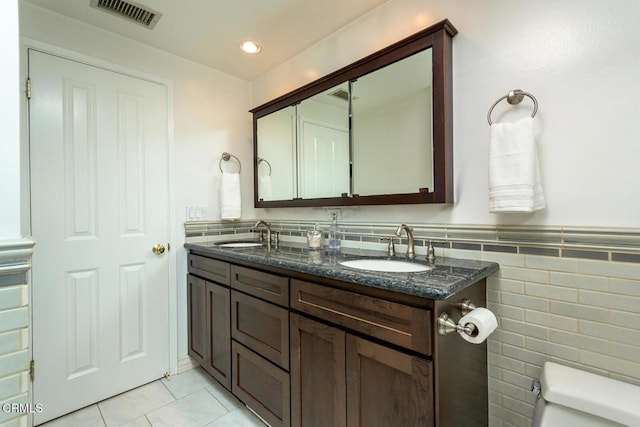 full bathroom with toilet, double vanity, visible vents, and a sink