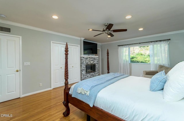 bedroom featuring a fireplace, crown molding, visible vents, light wood-style flooring, and baseboards