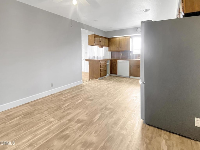 kitchen with brown cabinets, light wood finished floors, backsplash, freestanding refrigerator, and white dishwasher