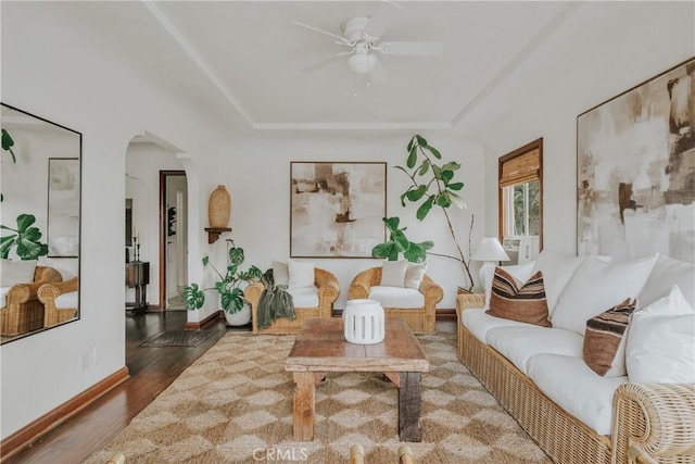 living room with wood finished floors, baseboards, arched walkways, ceiling fan, and a raised ceiling