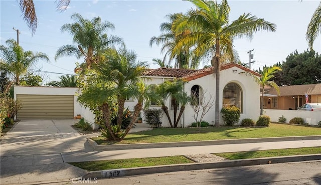 mediterranean / spanish house featuring a front lawn, a tiled roof, driveway, and stucco siding