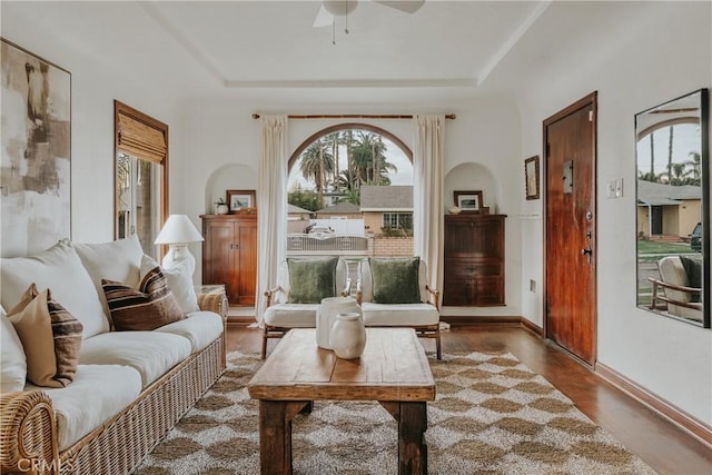 sitting room with ceiling fan, baseboards, a tray ceiling, and wood finished floors