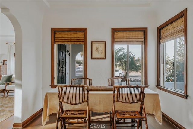 dining area with arched walkways, baseboards, and wood finished floors