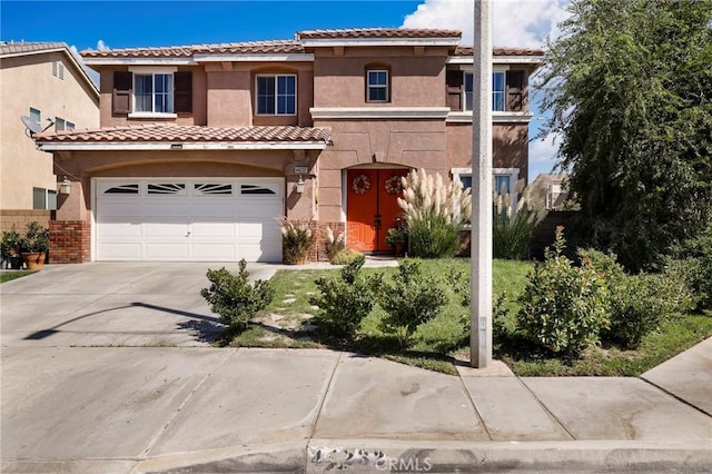 mediterranean / spanish-style home featuring a garage, concrete driveway, stucco siding, a tile roof, and brick siding