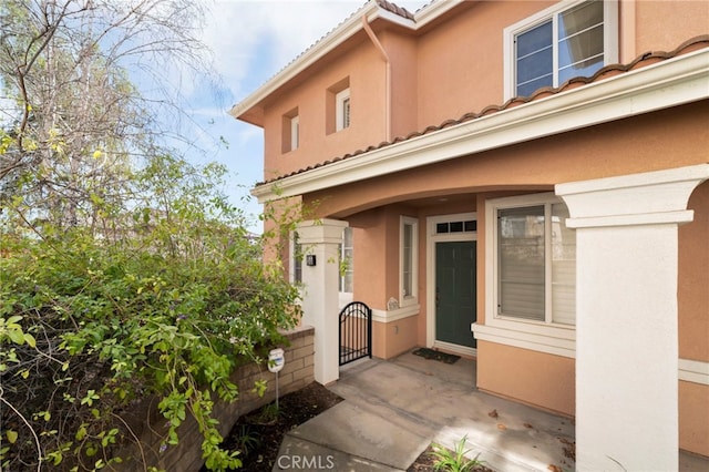 doorway to property with a gate, a tile roof, and stucco siding