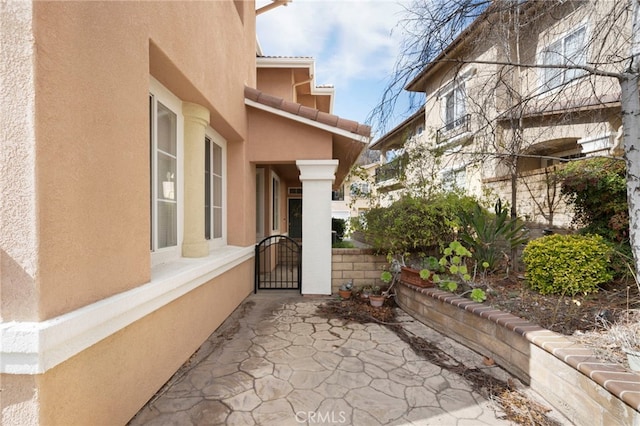 exterior space featuring a gate, a tile roof, and stucco siding