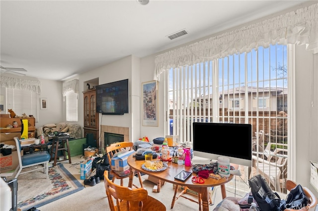 carpeted dining room with visible vents, ceiling fan, and a tiled fireplace