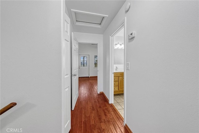 hall with attic access, a sink, baseboards, and wood finished floors