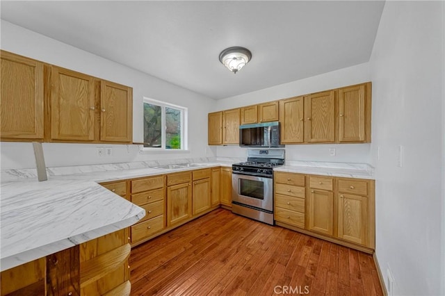 kitchen with a sink, stainless steel appliances, light countertops, and hardwood / wood-style flooring